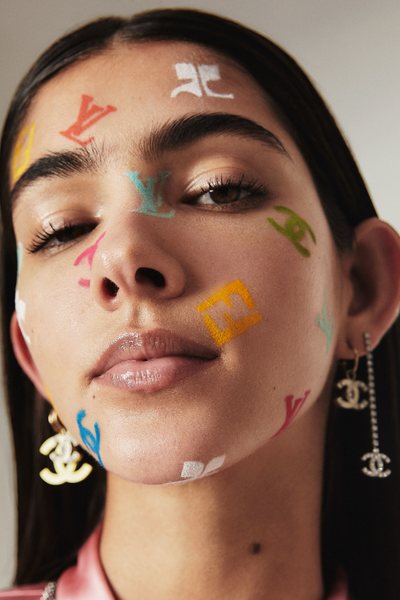 a young woman with face covered in make up presenting logos of various fashion houses