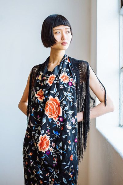 a model wearing an antique embroidered piano shawl by a window in a white and bright studio space