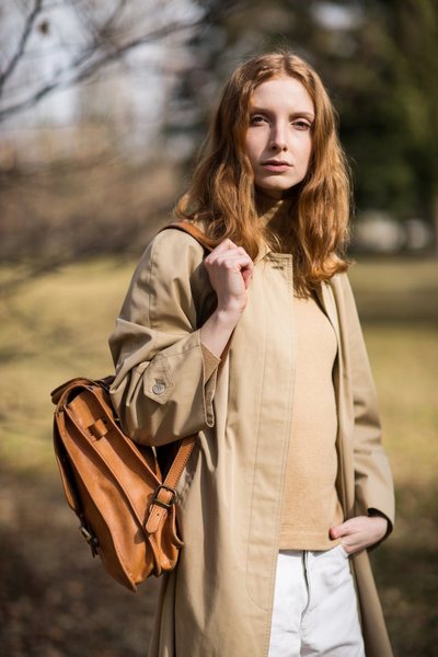 A young woman in a beige vintage trench coat, white jeans, and leather backpack.