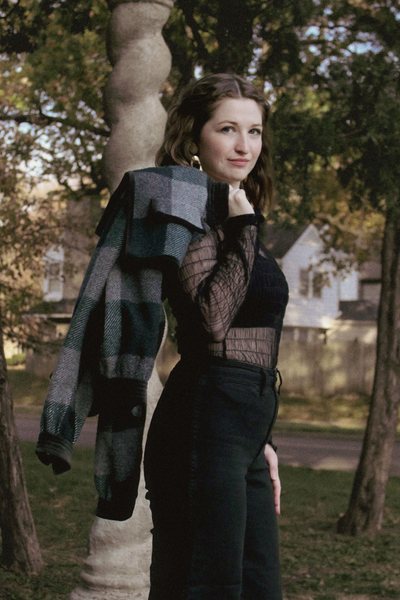 Brooke Bowlin photographed in a park wearing a black lace top, black high waisted pants and a plaid jacket