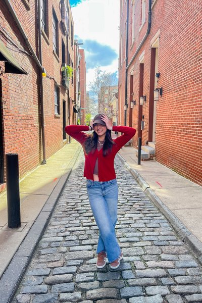 Bianca Lozano wearing a bright red thrifted cardigan, blue jeans and a cap