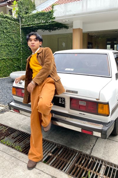 Indonesian Rayn Amrillah, 23, wearing a vintage outfit with a mustard yellow sweater vest, suede jacket and orange flare pants