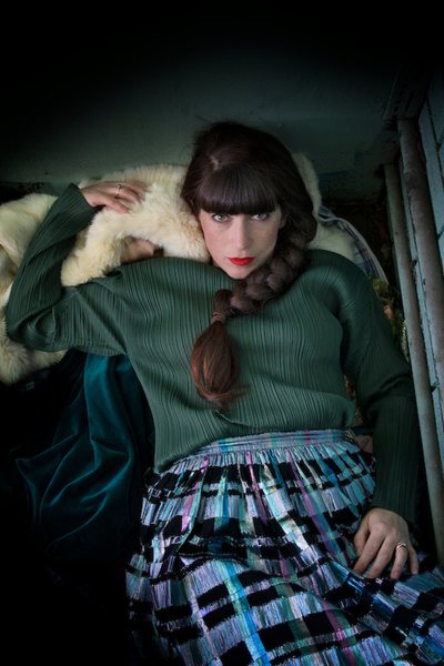 Sydney-based wardrobe stylist and slow fashion advocate Joanne Gambale in a dark green long sleeve vintage Pleats Please top and a plaid metallic skirt in blue, black and purple colors.