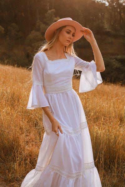 A model in the field in the sunset, wearing a white vintage 70s Mexican style wedding gown.