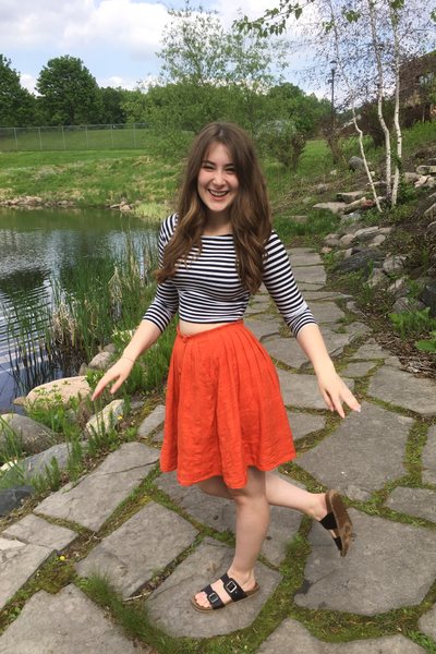 Gabrielle Jones wearing a thrifted secondhand orange midi skirt with black-and-white striped long sleeve top and Birkenstocks