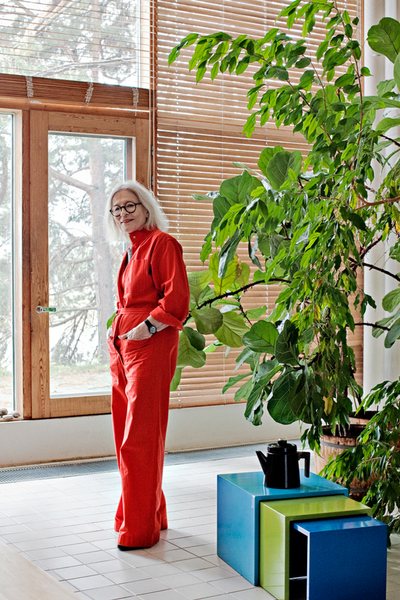 Designer Vuokko Nurmesniemi in her studio home, wearing a bright red Vuokko jumpsuit.