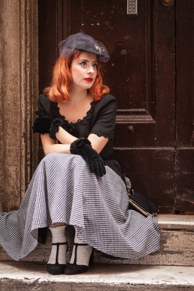 Carolina Cominelli, 25, sitting on a doorstep, wearing a black-and white vintage outfit