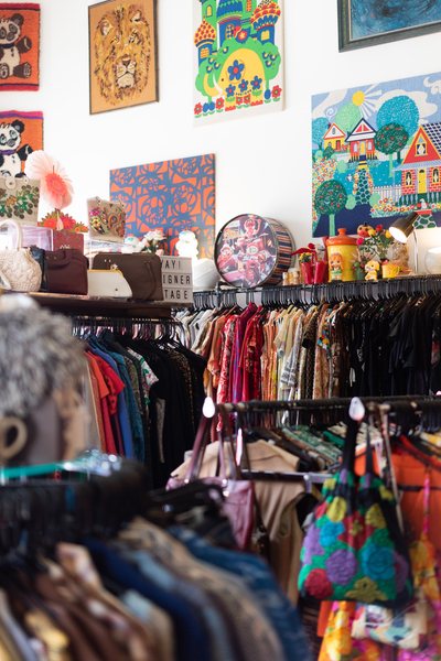 interior photo of the very Best Vintage store in Chicago; lots of tightly packed clothing racks and 60s 70s style paintings and posters on the wall