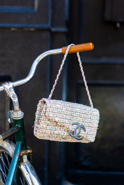 a Chanel tweed flap bag with a big CC logo hanging on a bicycle handle