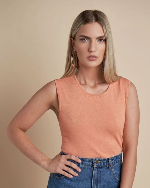 a young woman wearing a peach colored sleeveless top