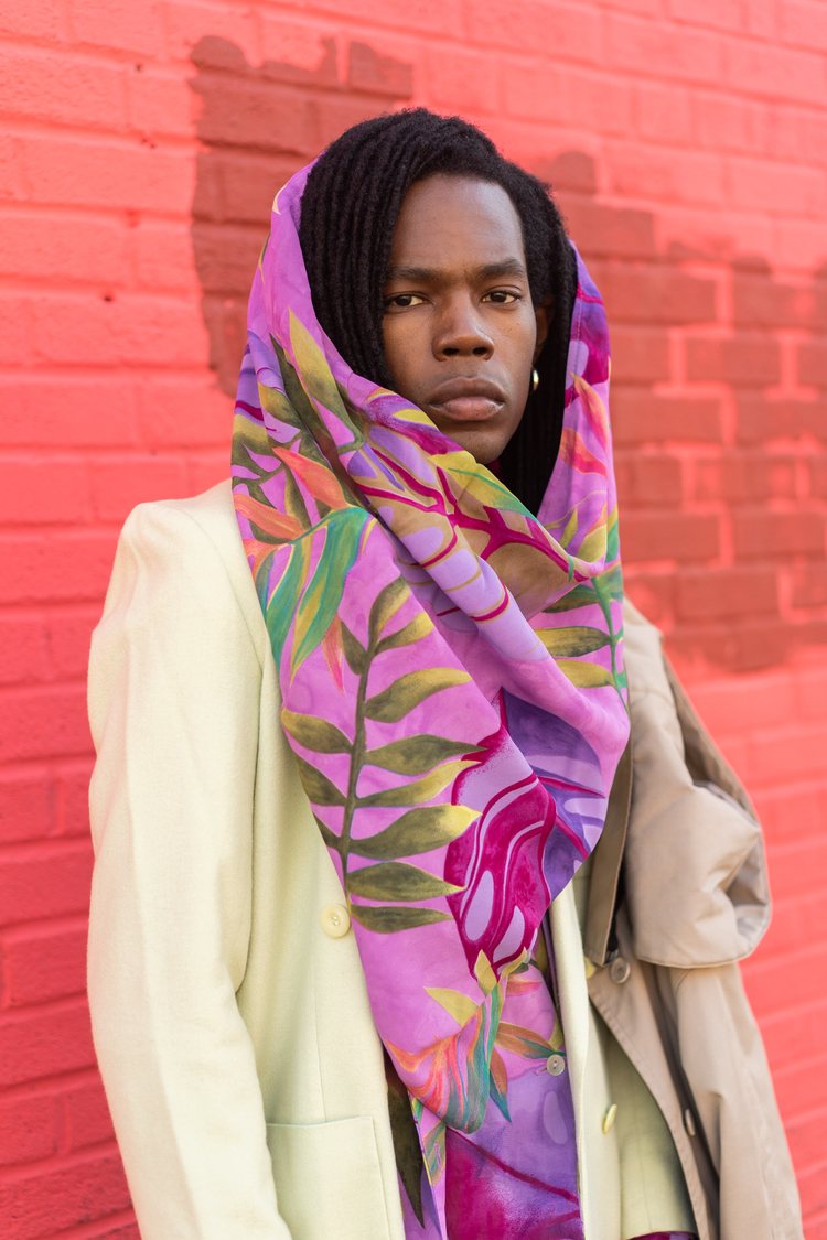 Stylist and model Eric Ellison in a pale green vintage blazer and a purple printed vintage scarf wrapped loosely around his head. Another vintage blazer is hanging from his shoulder.