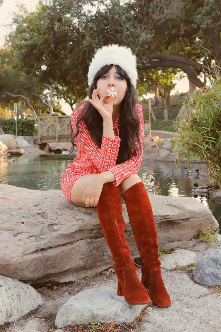 Larissa Blintz, 24, the owner and designer of Miracle Eye, sitting in a park on a rock, wearing a vintage 60s fur hat, 60s mini dress and suede go go boots.