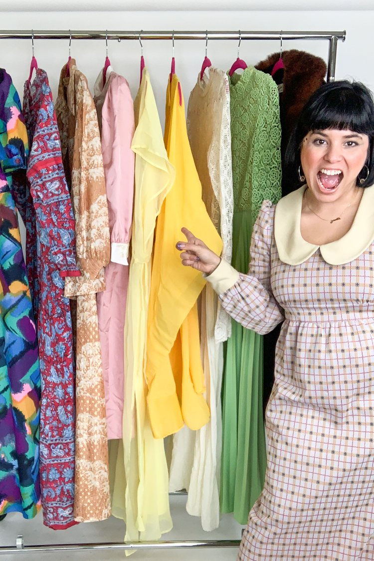 Monique Danielle Gatillon of LA Retro Girl in front of her colorful clothing rack. There are 50s, 60s, and 70s vintage dresses on the rack.