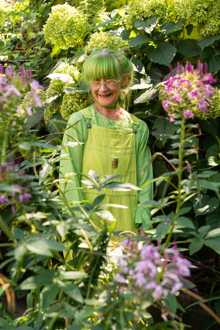 smiley Elizabeth Sweetheart, 78, aka The Green Lady of Brooklyn standing in the middle of her green lush garden, wearing green frames, green long sleeve shirt and green overalls