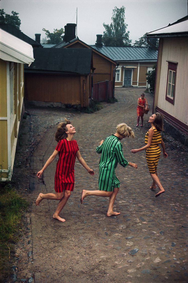 three models in striped Marimekko cotton dresses dancing barefeet in the cobble stone street in the old town of Porvoo in 1964